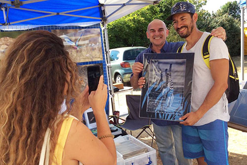 photographer Ashley Vincent and a customer holding a wildlife print he has just purchased while his girlfriend take a photograph of them