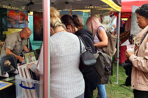 ladies looking through wildlife prints at an outdoor event while photographer Ashley Vincent deals with a customer