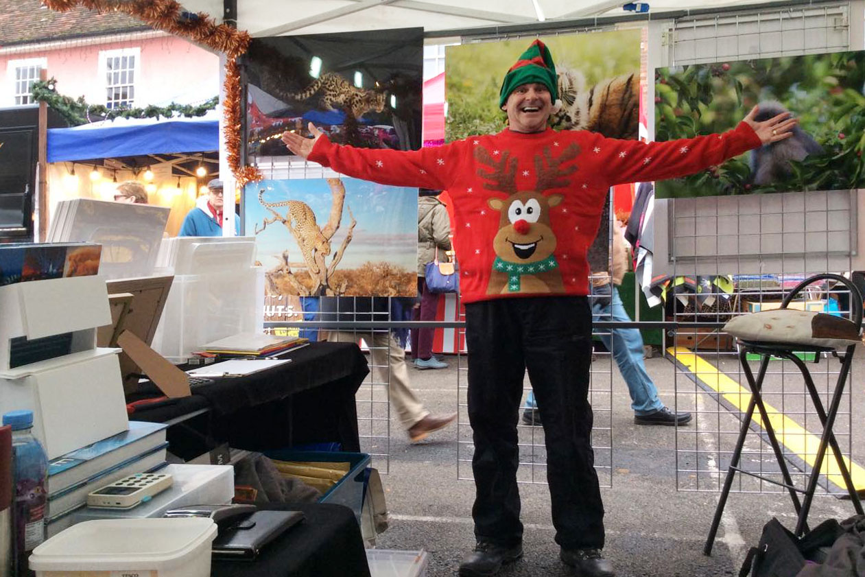 wildlife photographer Ashley Vincent in his event stand wearing a Christmas jumper and a big smile with arms stretched out wide